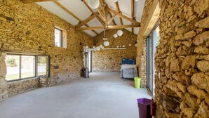 Una habitación de paredes de piedra con techo alto, vigas de madera, un ventanal grande y un recipiente metálico.