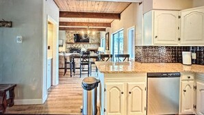 A modern kitchen with wooden beams, a stone backsplash, and a dining area with bar stools. - 'Enchanted Pines' Mountain Escape! (Angel Fire)