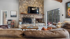 A living room with a stone fireplace, a large flat-screen TV, and a cozy seating area. - 'Enchanted Pines' Mountain Escape! (Angel Fire)