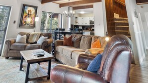 A spacious living area with a high ceiling, wooden beams, a staircase, and a view of the outdoors. - 'Enchanted Pines' Mountain Escape! (Angel Fire)