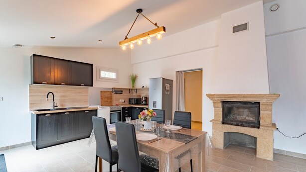 A modern kitchen with dark cabinets, a central island, and a dining area with a table and chairs.