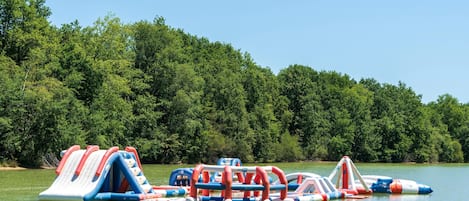 Un parque acuático inflable con toboganes y estructuras de juego en un lago rodeado de árboles.