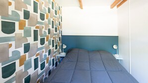 A bedroom with a geometric-patterned wall, a bed with a grey duvet, and bedside tables with lamps. - Chalet 'Club 5 Personnes 89' with Private Terrace, Private Garden and Wi-Fi (Bretagne-d'Armagnac)