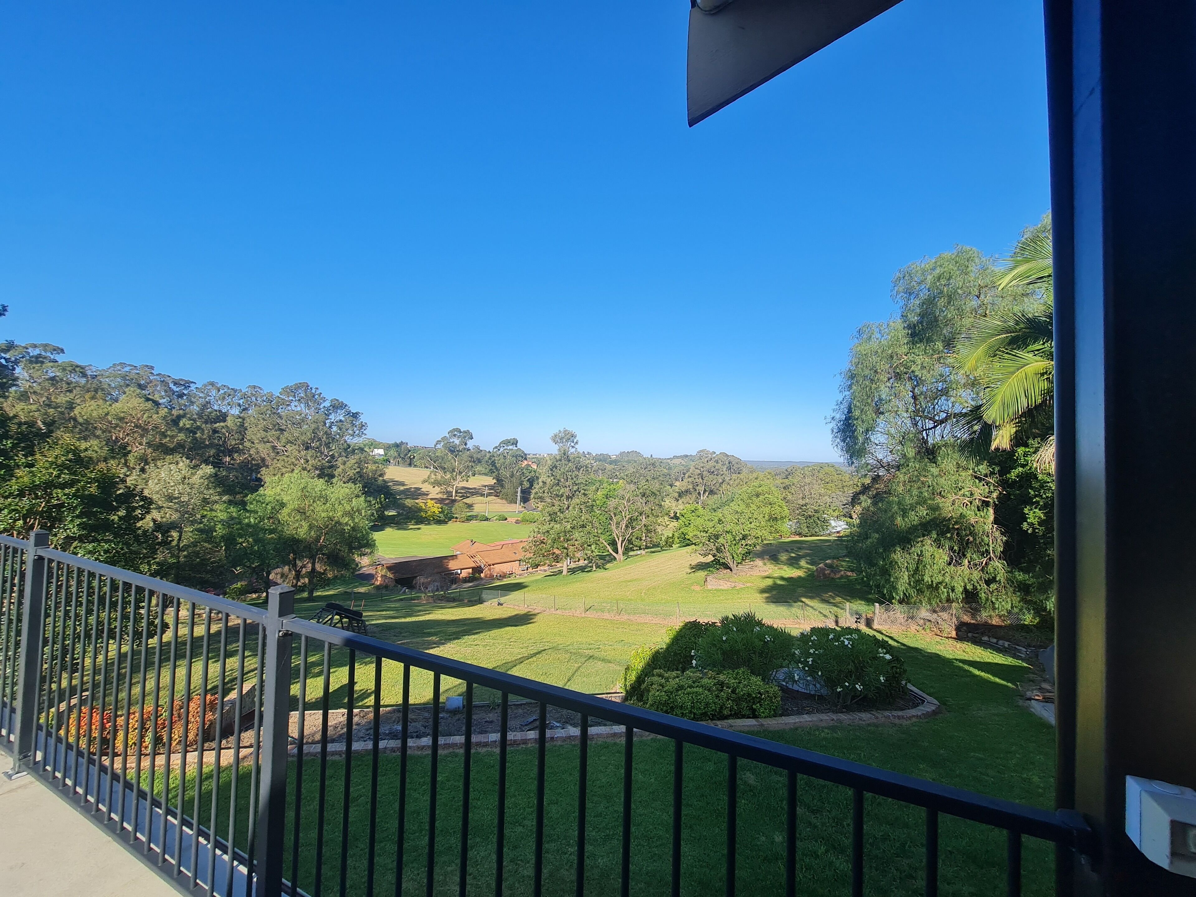 A balcony with a clear view of a well-maintained lawn and distant hills.