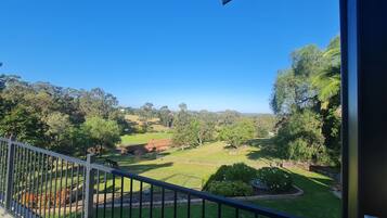 A balcony with a clear view of a well-maintained lawn and distant hills.