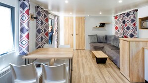 A modern RV interior with a dining area, a sofa, and a small table. - Mobile Home 'Mobilhome Confort 4 Personnes 63' with Private Terrace, Private Garden and Wi-Fi (Bretagne-d'Armagnac)