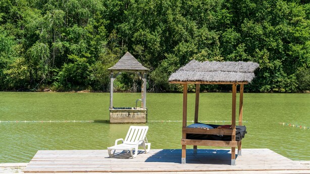 A wooden dock with a thatched-roof gazebo, a white lounge chair, and a small docked boat. - Mobile Home 'Mobilhome Confort 4 Personnes 63' with Private Terrace, Private Garden and Wi-Fi (Bretagne-d'Armagnac)