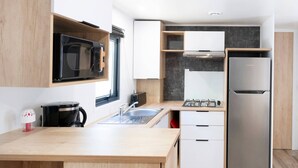 A modern kitchen with a microwave, stove, sink, and refrigerator. - Mobile Home 'Mobilhome Confort 4 Personnes 63' with Private Terrace, Private Garden and Wi-Fi (Bretagne-d'Armagnac)