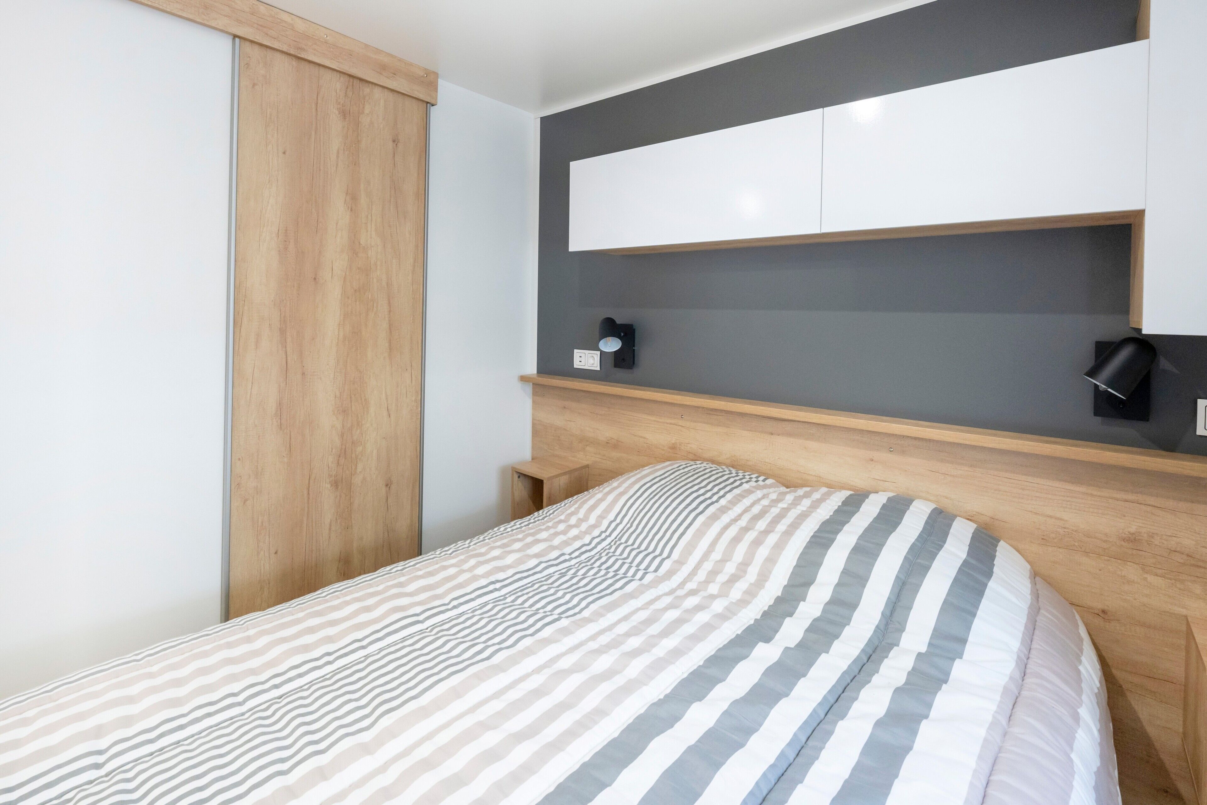 A bedroom with a bed, wooden headboard, built-in shelves, and a bedside table.