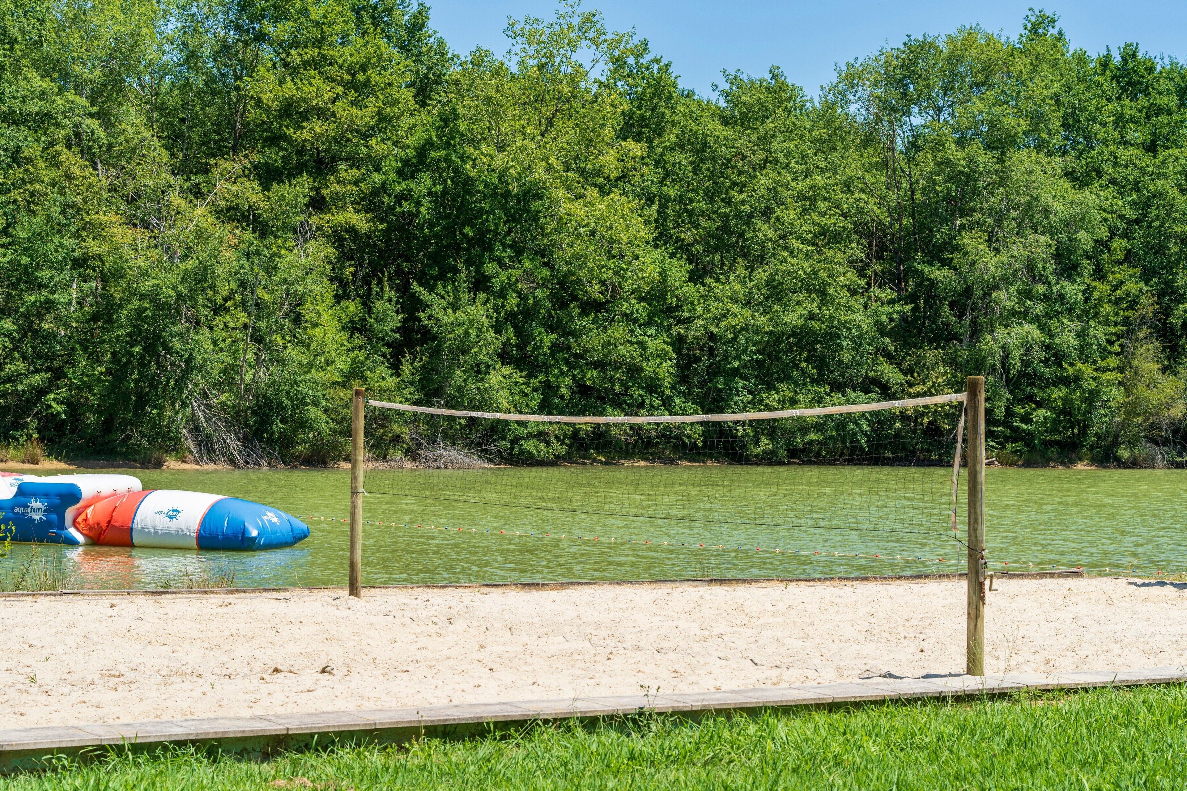 A sandy beach with a volleyball net and inflatable water toys.