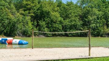 A sandy beach with a volleyball net and inflatable water toys.