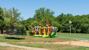 Una estructura inflable con temática pirata, que incluye toboganes y zonas de escalada, rodeada por un campo de césped y árboles.