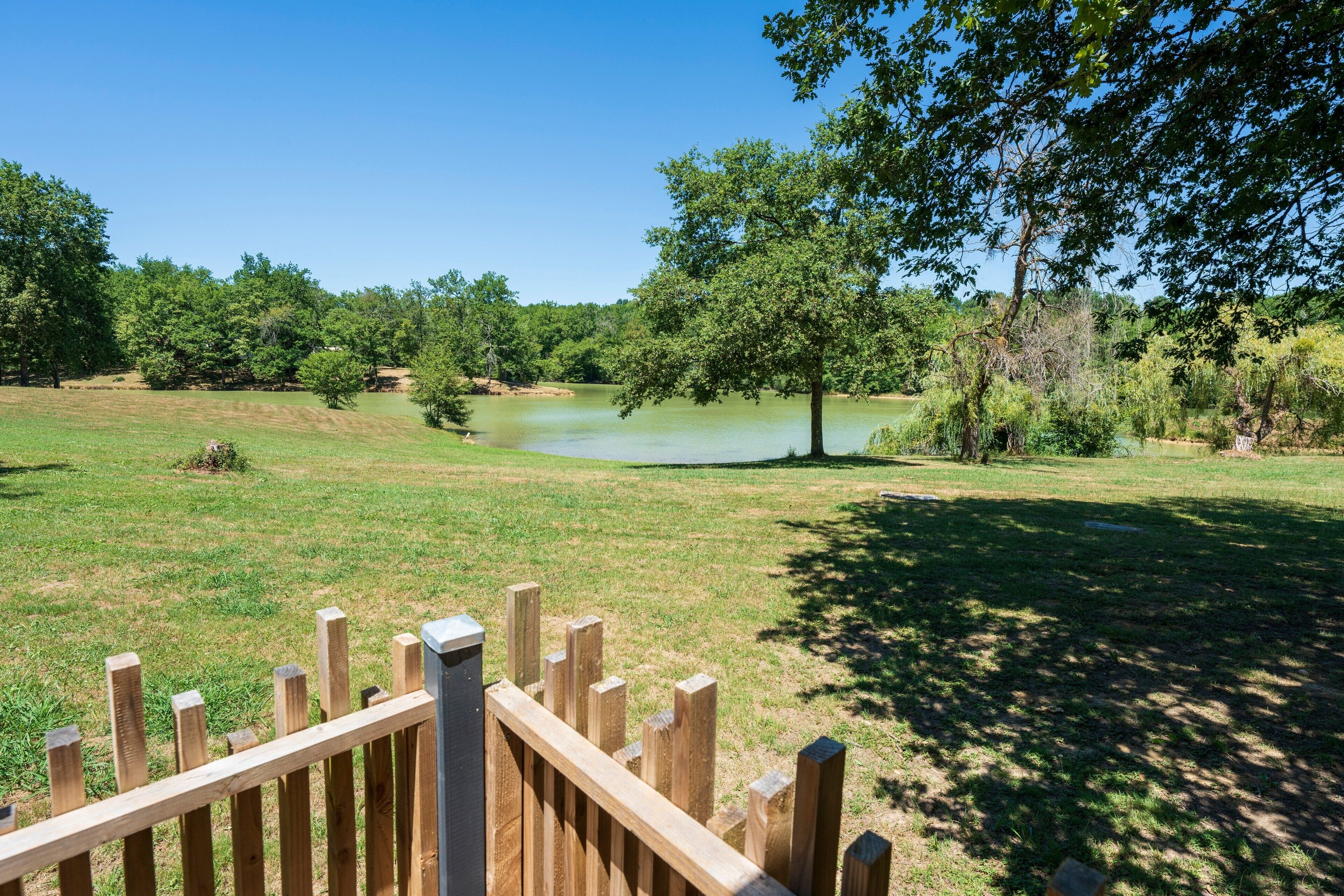A grassy area with a pond, trees, and a wooden fence.