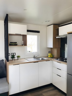 A modern kitchen with white cabinets, a stainless steel sink, a window, and a stove.
