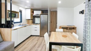 A compact kitchen with white cabinets, a microwave, a stove, and a refrigerator. There is a dining area with a wooden table and white chairs.