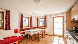 Ein gemütliches Zimmer mit Holzboden, einem roten Sofa, einem Esstisch mit Stühlen und einer Küchenzeile mit Schränken und einer Kaffeemaschine.