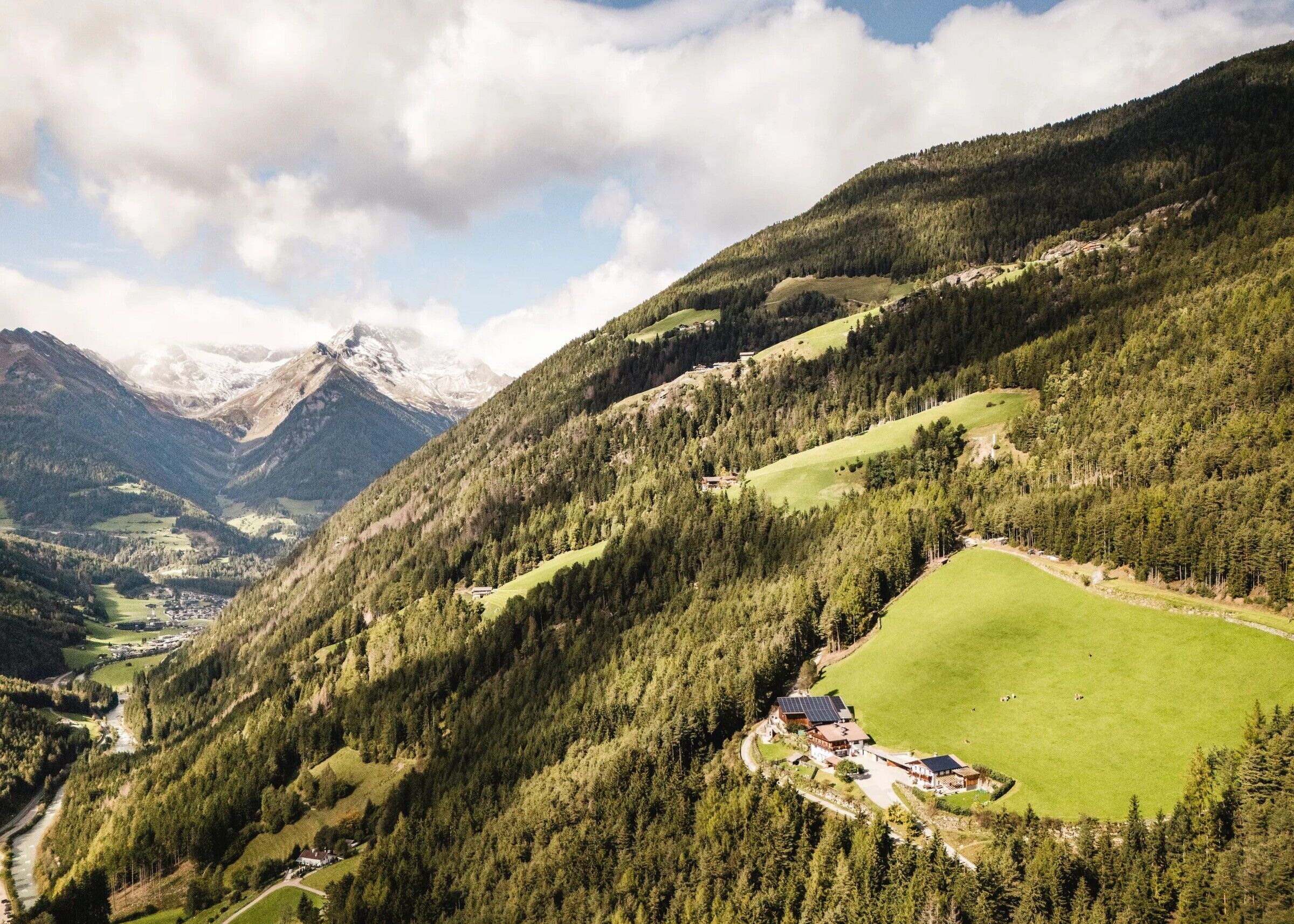 Bergachtig landschap met een vallei, een rivier en een kleine nederzetting met gebouwen en een huis met zonnepanelen.