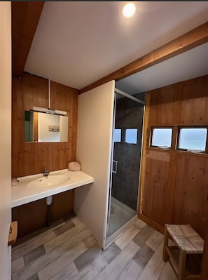 A bathroom with wooden walls, a white sink, and a glass shower door.