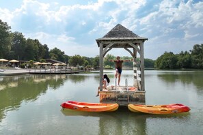 A gazebo structure with a platform extending over water, surrounded by canoes and a dock area with umbrellas.