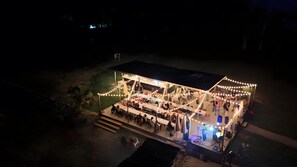 An outdoor venue with a stage, tables, and chairs, surrounded by string lights.