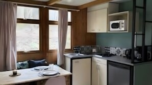 Una cocina compacta con microondas, pileta y placares. Cuenta con una mesa de comedor con sillas y un ventanal con cortinas.