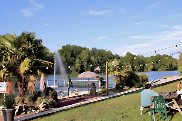Un patio junto al lago con sillas, una mesa, un pabellón y una fuente.