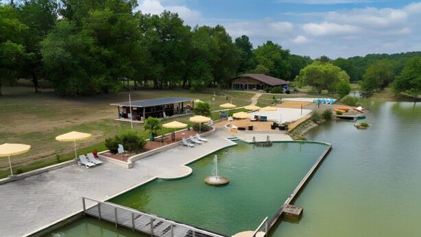 A swimming pool with a fountain, surrounded by lounge chairs and umbrellas, with a building in the background.