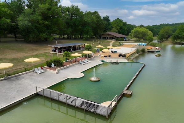 A swimming pool with a fountain, surrounded by lounge chairs and umbrellas, with a building in the background.