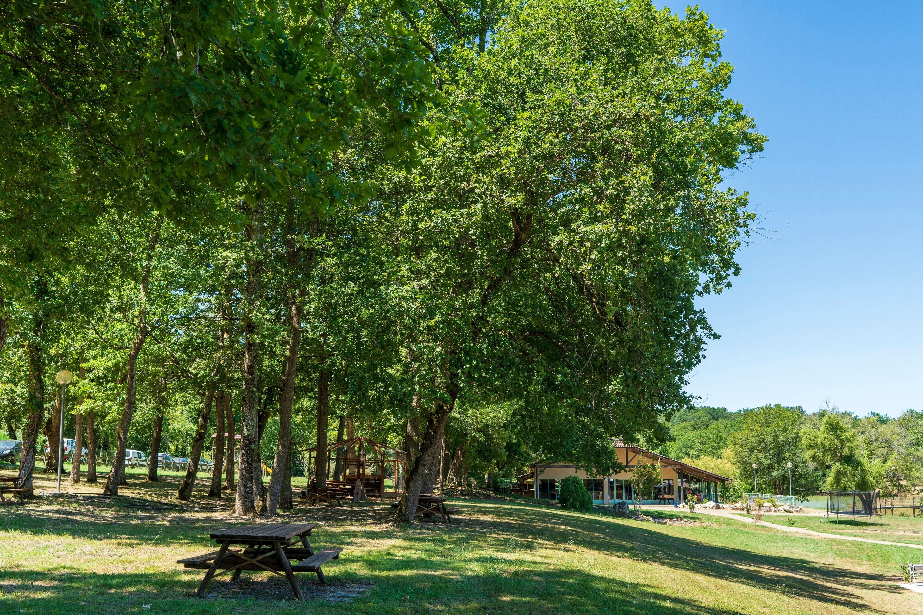 Un parco con tavoli da picnic, un edificio con tetto spiovente e cielo sereno.