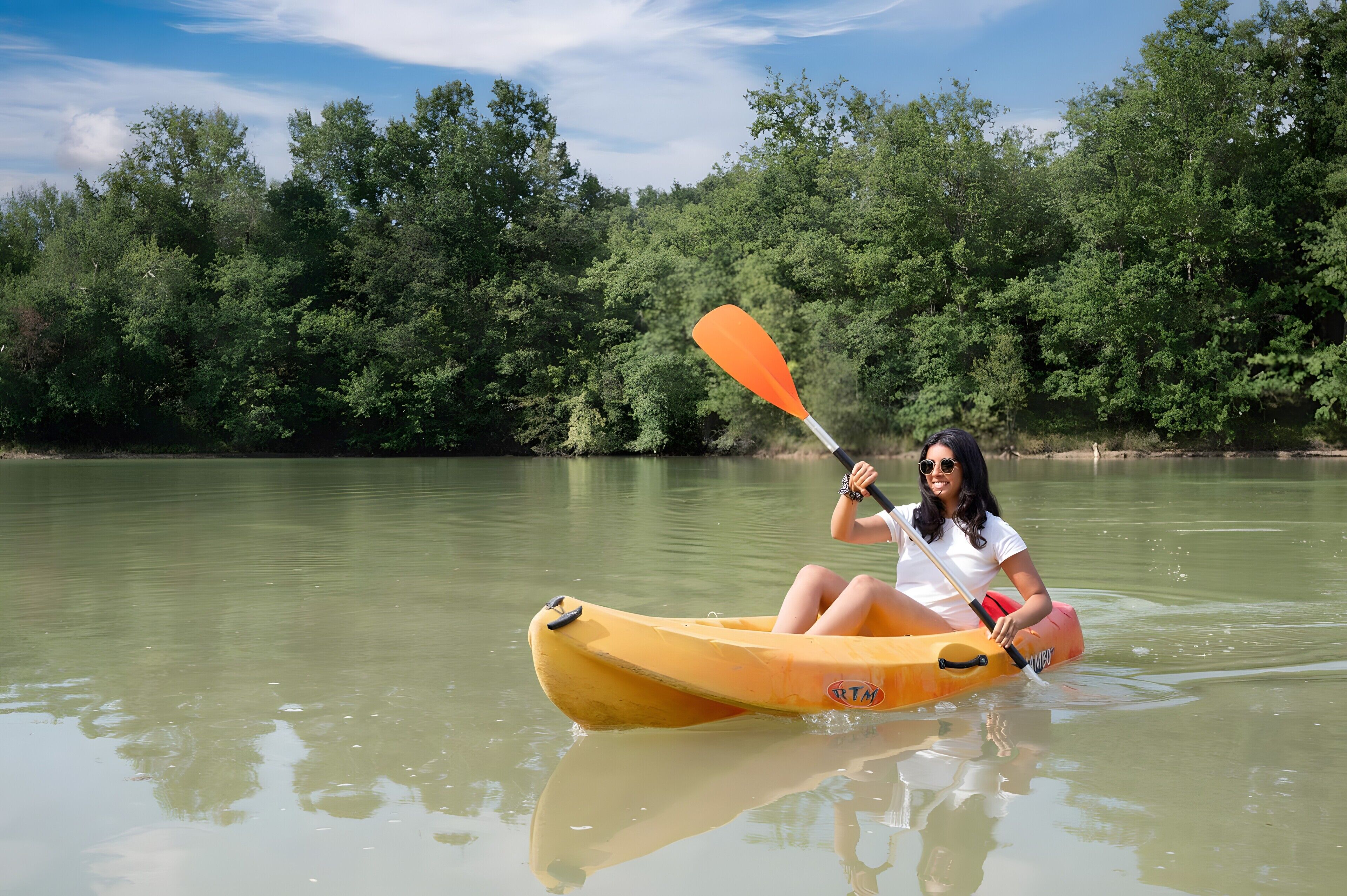 A person in a yellow kayak on a calm river surrounded by dense green trees.