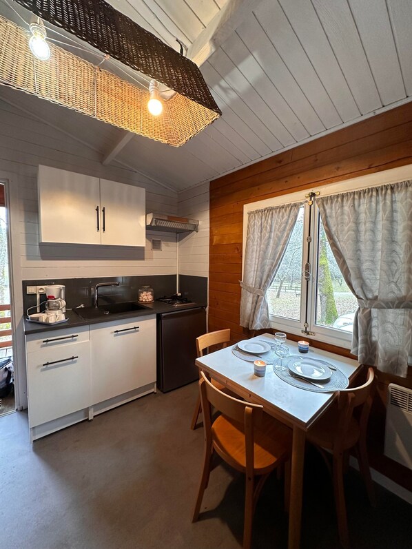 A compact kitchen with white cabinets, a black countertop, and a dining area with a table set for two.