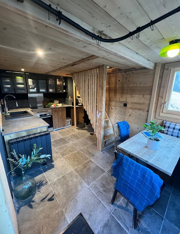 Una cocina con electrodomésticos modernos, un comedor con mesa y sillas, y una separación de madera.