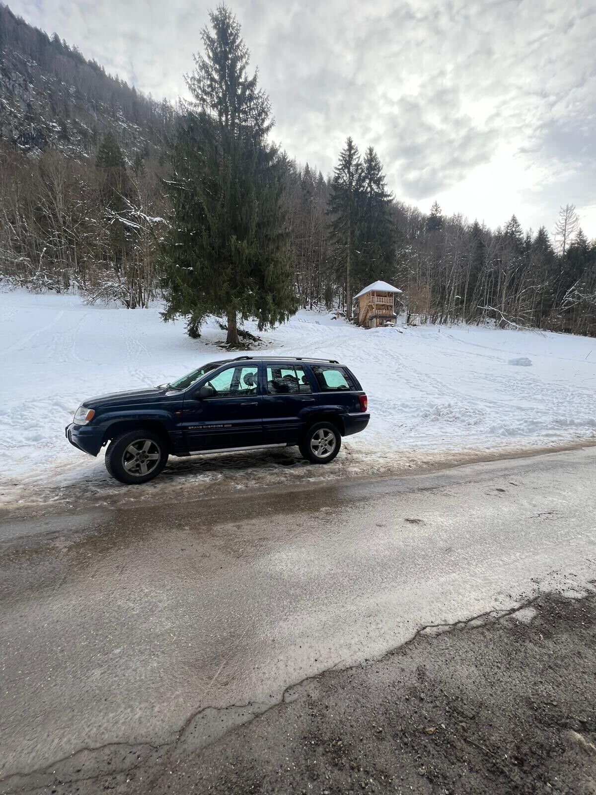 Un SUV negro estacionado en una carretera cubierta de nieve, con una cabaña de madera al fondo.