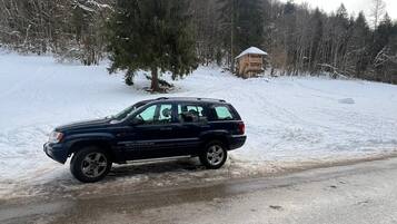 Un SUV negro estacionado en una carretera cubierta de nieve, con una cabaña de madera al fondo.