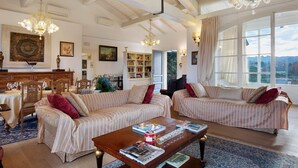 A spacious living room with two sofas, a coffee table, and a chandelier. There is a dining area with a table and chairs, and a bookshelf filled with books. - Villa 'La Provenzale' with Mountain Views, Wi-Fi and Air Conditioning (Camaiore)