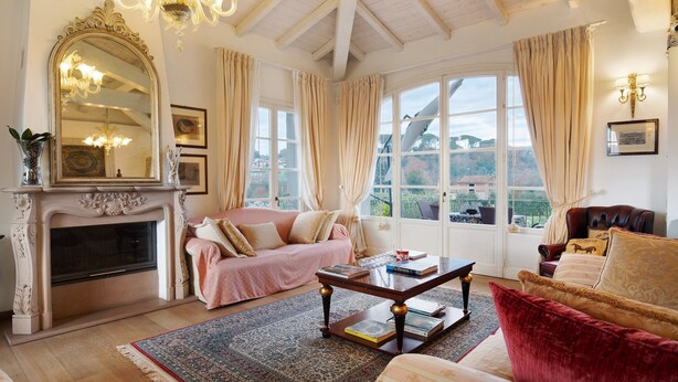 A room with a fireplace, a sofa, a red armchair, a coffee table, and a large window with curtains. - Villa 'La Provenzale' with Mountain Views, Wi-Fi and Air Conditioning (Camaiore)