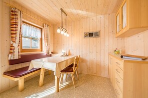 Puinen mökki, jonka sisustuksessa on ruokapöytä, penkki ja kaappeja.