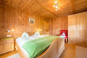 Quarto com paredes de madeira, uma cama, mesas de cabeceira, uma cadeira vermelha e um guarda-roupa.