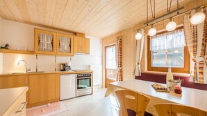 Un interior de madera con cocina, comedor y una ventana con cortinas.