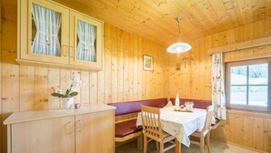 Una cabaña de madera con comedor que incluye un banco, mesa, sillas y una ventana con vistas.