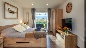 A modern bedroom with a wooden bed, a TV, and a large window with a view of greenery.
