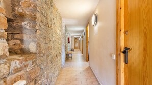 A corridor with stone walls, wooden doors, and a tiled floor.