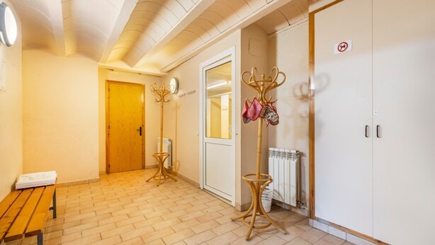 Un couloir avec un banc en bois, une porte, un radiateur et un porte-manteau avec des chapeaux.