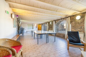 A room with a long table, wicker chairs, a stone wall, and a window with curtains.