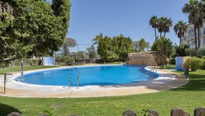 Una piscina con un deck de piedra, rodeada de césped y árboles.