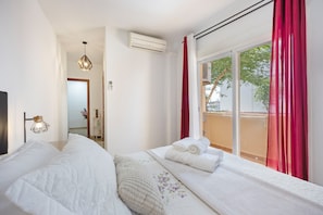 Une chambre d’hôtel avec un lit, une fenêtre avec des rideaux rouges, un appareil de climatisation et un luminaire suspendu.
