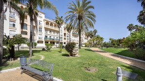 Un patio de hotel con un sendero empedrado, un banco de metal, palmeras y una escultura de piedra.