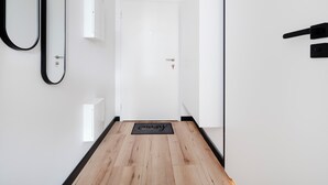 A hallway with a wooden floor, a black doormat, a white door, and a mirror on the left wall. - Platon 46 Modern Studio (Łódź)