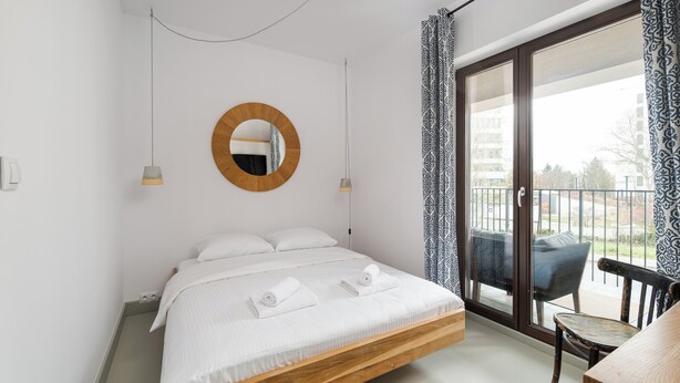 A bedroom with a wooden bed, a round mirror, and a balcony with patterned curtains. - Tolkiena Charming Apartment (Warszawa)