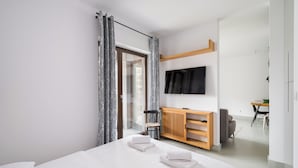 A modern hotel room with a large bed, a TV mounted on the wall, a wooden console table, and a dining area in the background. - Tolkiena Charming Apartment (Warszawa)